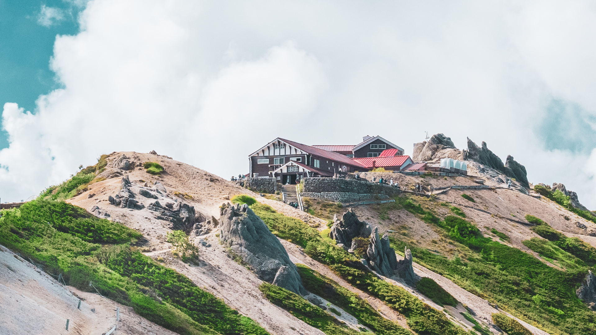 山の頂上付近に建つ、山小屋。建物の周りは岩や低木に覆われている。